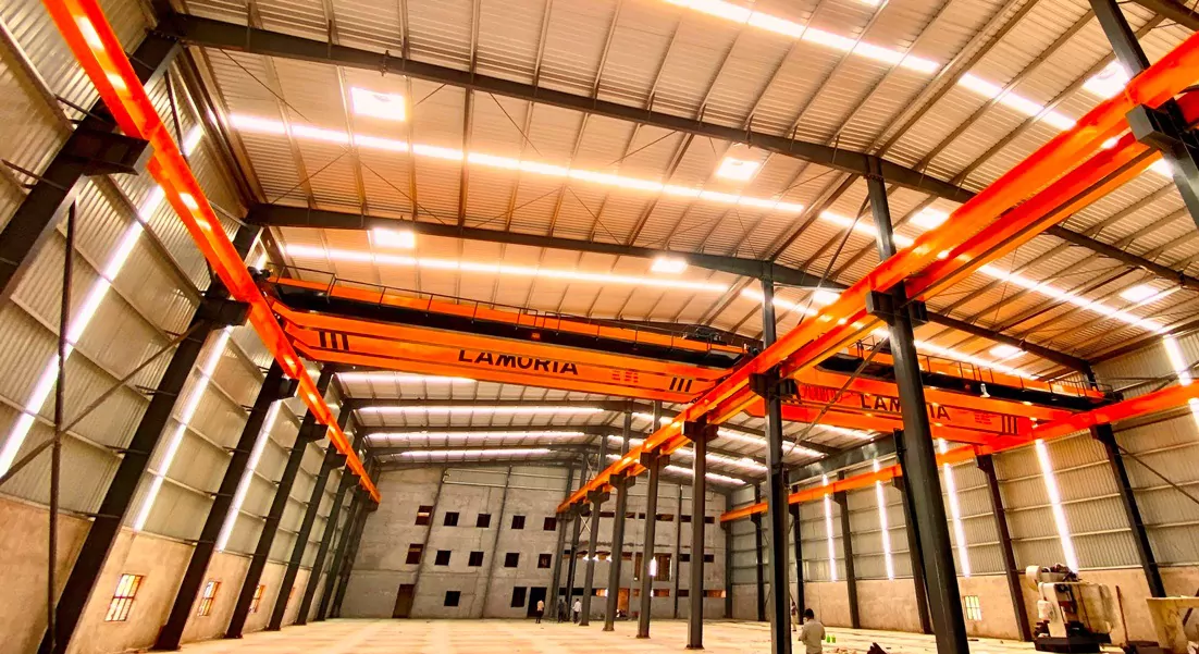 Completed pre-engineered steel warehouse interior with orange overhead gantry cranes, Krishnan Metals PEB project
