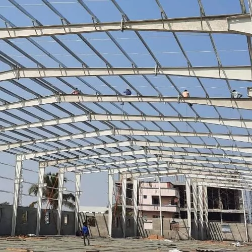PEB steel frame erection at a site with an RCC commercial building under construction in the background