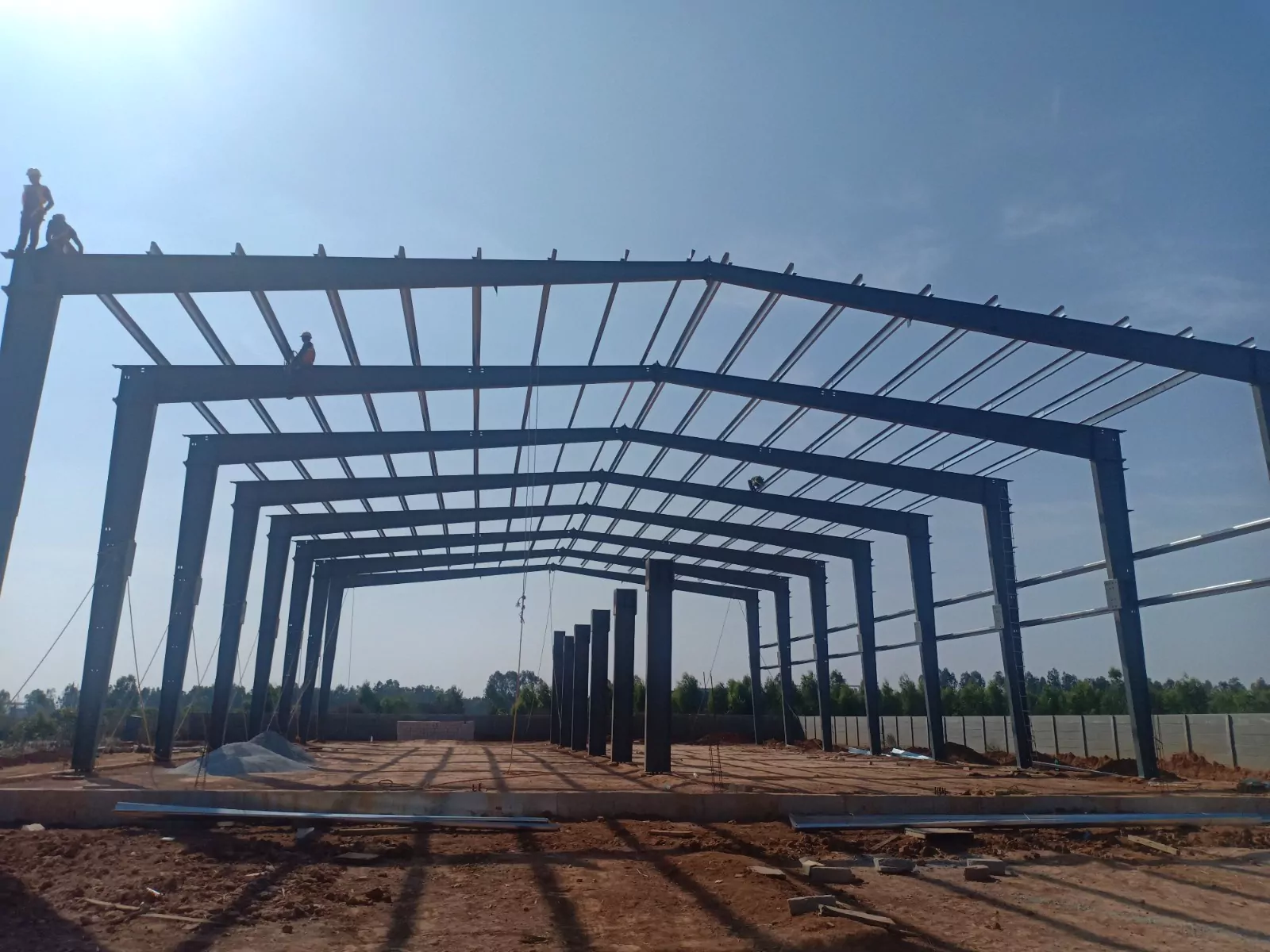 Workers in safety gear installing steel purlins during pre-engineered building erection